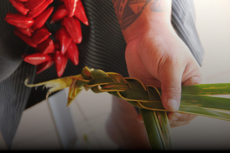 Photo of a Samoan person's hands weaving a headband from palm leaves.